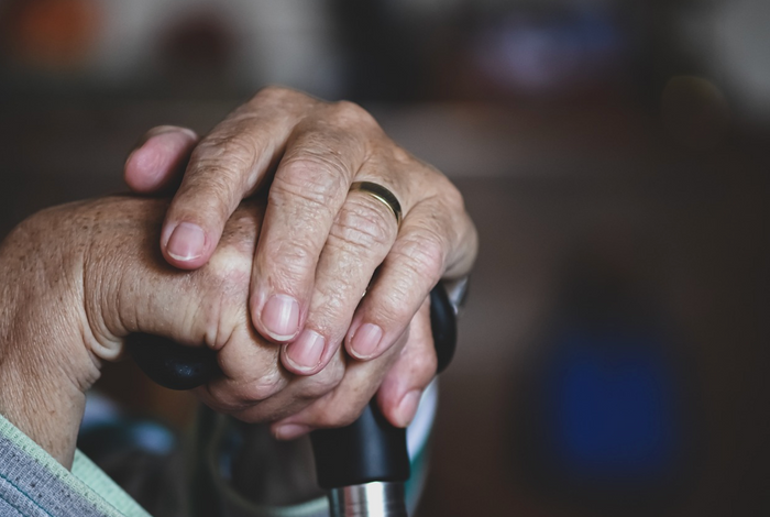 Close-up of a person's hands resting on the handle of a cane
